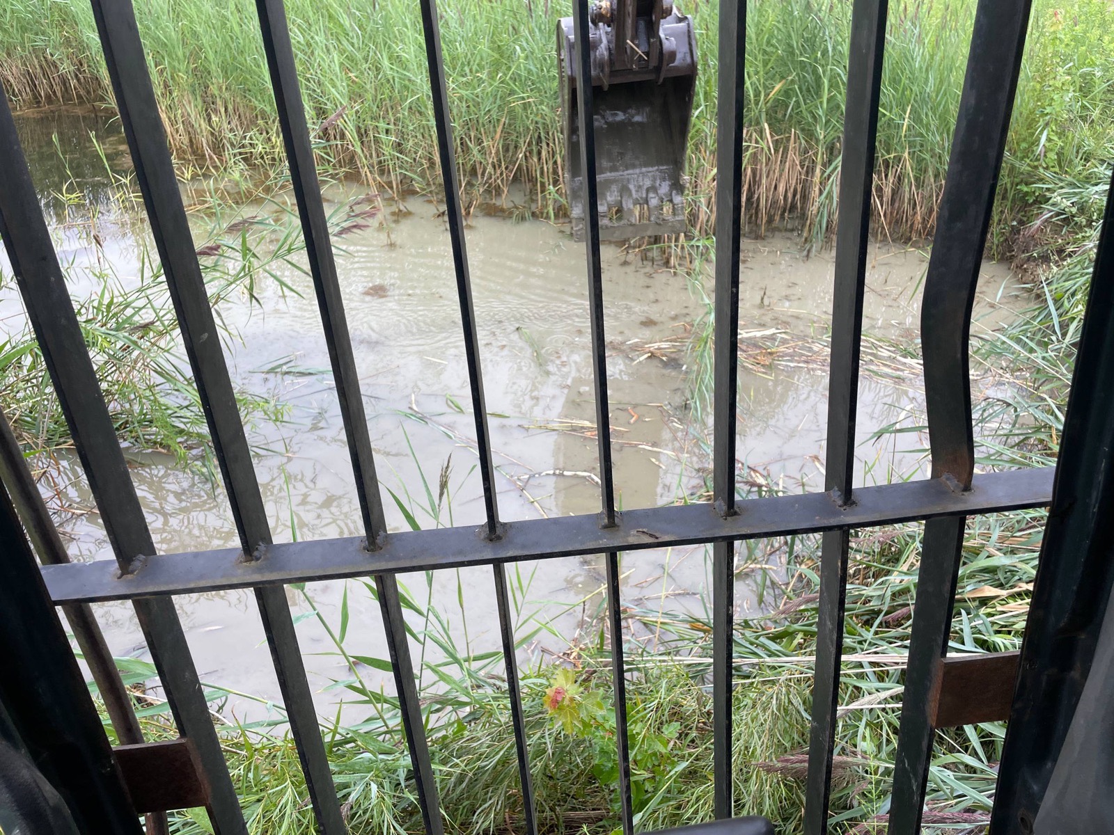 During — operator's view from the cab, bucket working muck at the water's edge — Brohez Trucking LLC